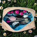 Open crèmekleurige gewatteerde La Lunore Buttercup toilettas met lichtblauwe voering, gevuld met stylingtools en opzetstukken.