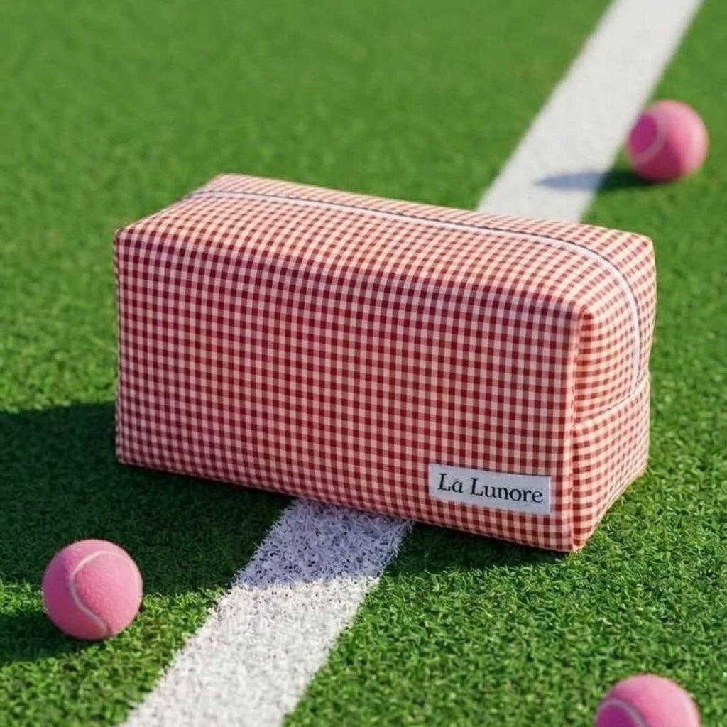 Rood-wit geruite La Lunore toilettas met wit merklogo op groen kunstgras met roze tennisballen.