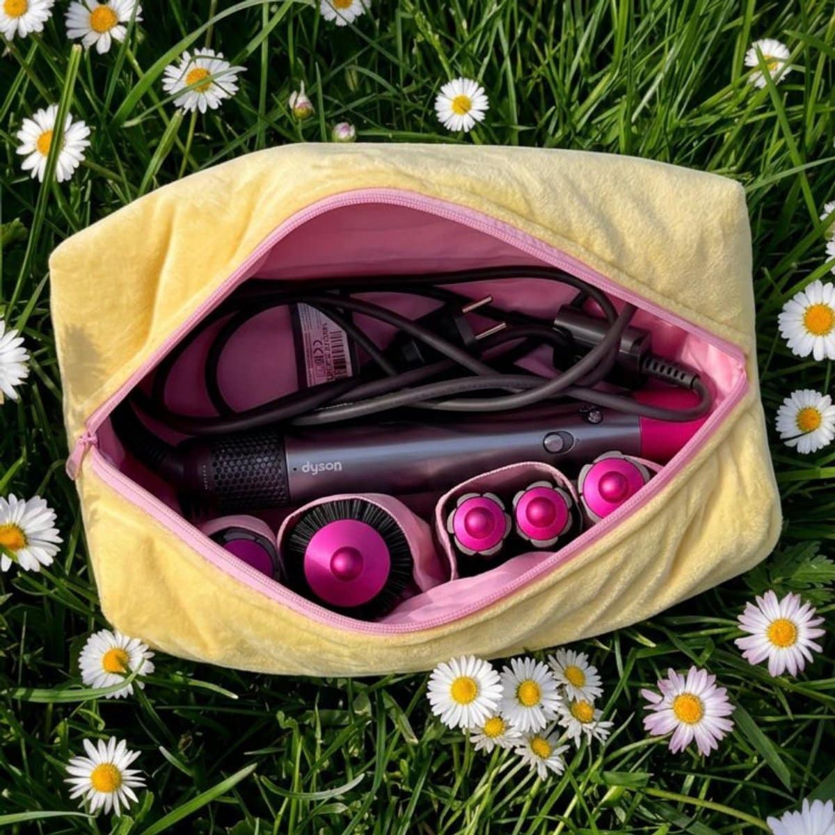 Gele en roze La Lunore Sunshine toilettas met velvet afwerking, gesloten met roze rits, op zand met citroen en handdoek.